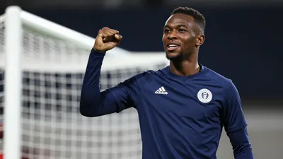 A 25-year-old Congolese-Dutch winger in a dark blue training kit, waist-up, celebrating a goal with a fist pump