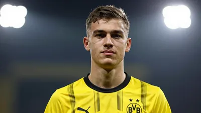 A 20-year-old left-back in a Borussia Dortmund jersey, with a confident expression, looking directly at the camera, with...