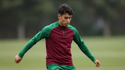 A focused, waist-up portrait of a 22-year-old forward mid-action, his face intense and eyes locked on the ball, dark red...