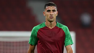 Mid-20s, sturdy midfielder, dark red and green plain training top, sleeves tucked, sweat-glazed skin, intense eyes fixed...